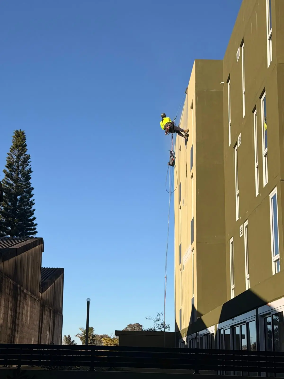 Rope access technician working on the rendered façade of a 4-storey residential building in Mascot