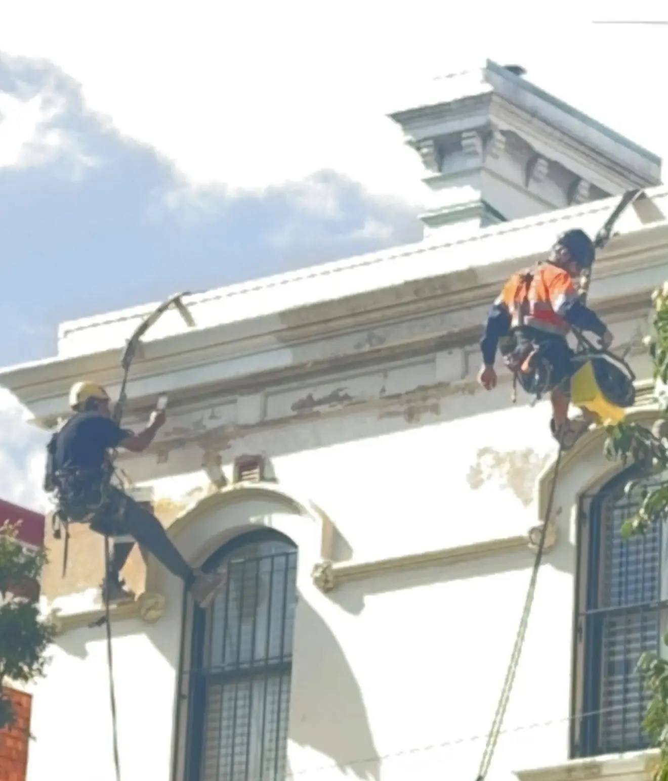 Two painters on rope preparing the cornice of a heritage terrace in Redfern for repainting
