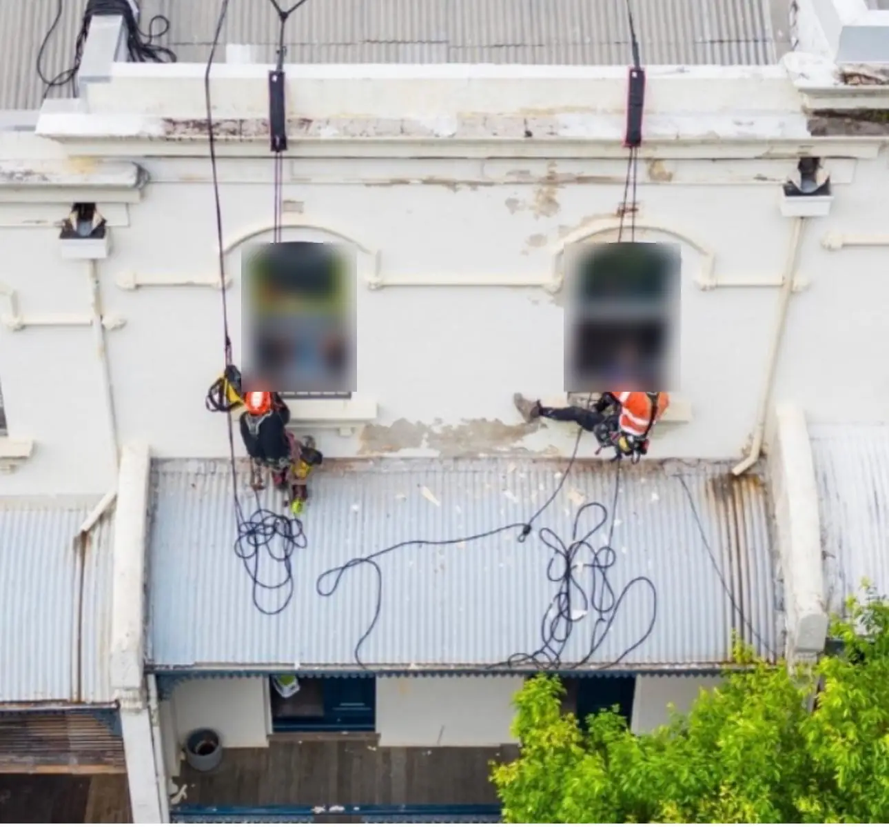 Two technicians on rope repairing the heritage façade above the street awning in Redfern